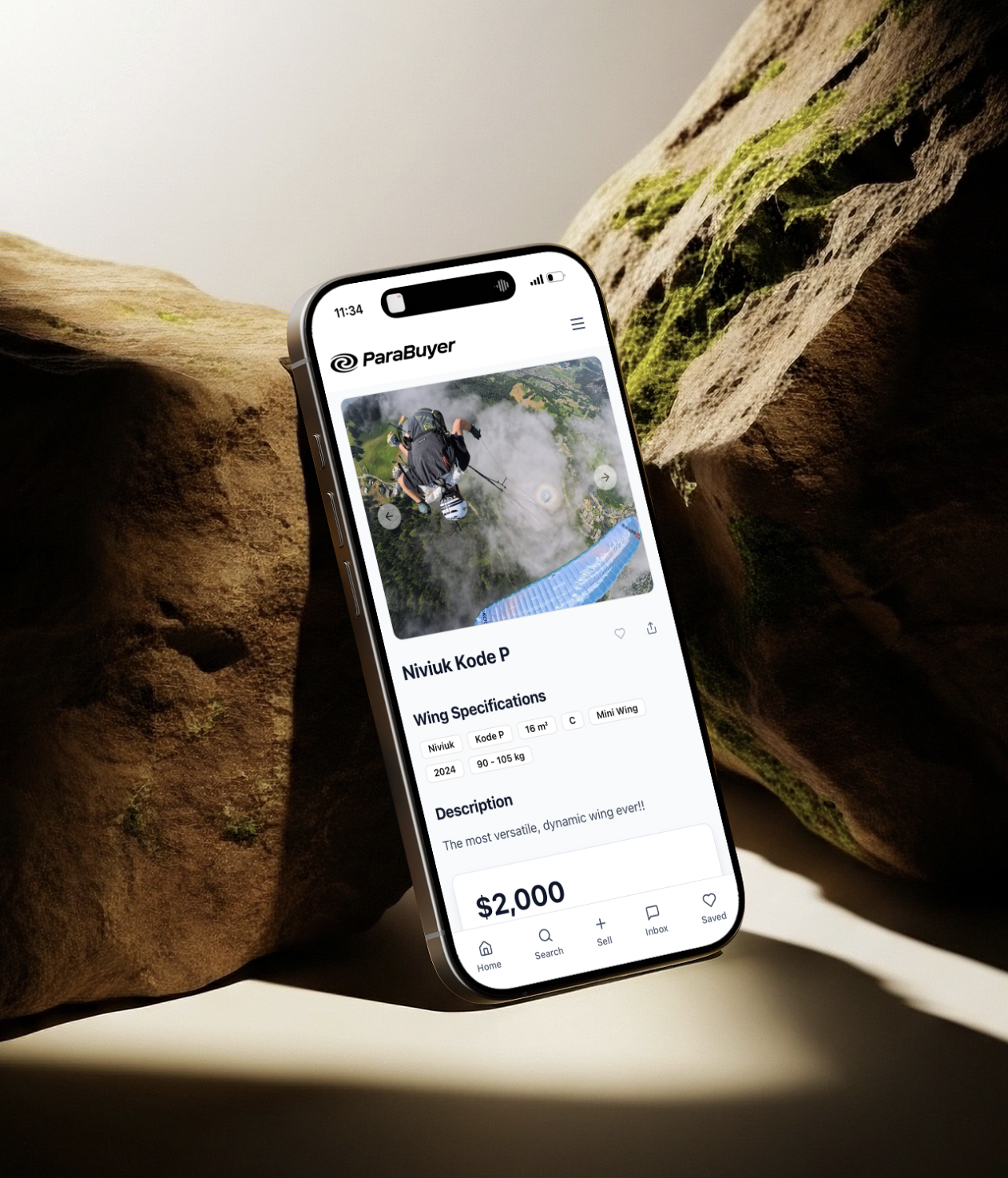ParaBuyer listing detail screen — Niviuk Kode P wing — on iPhone propped between mossy rocks