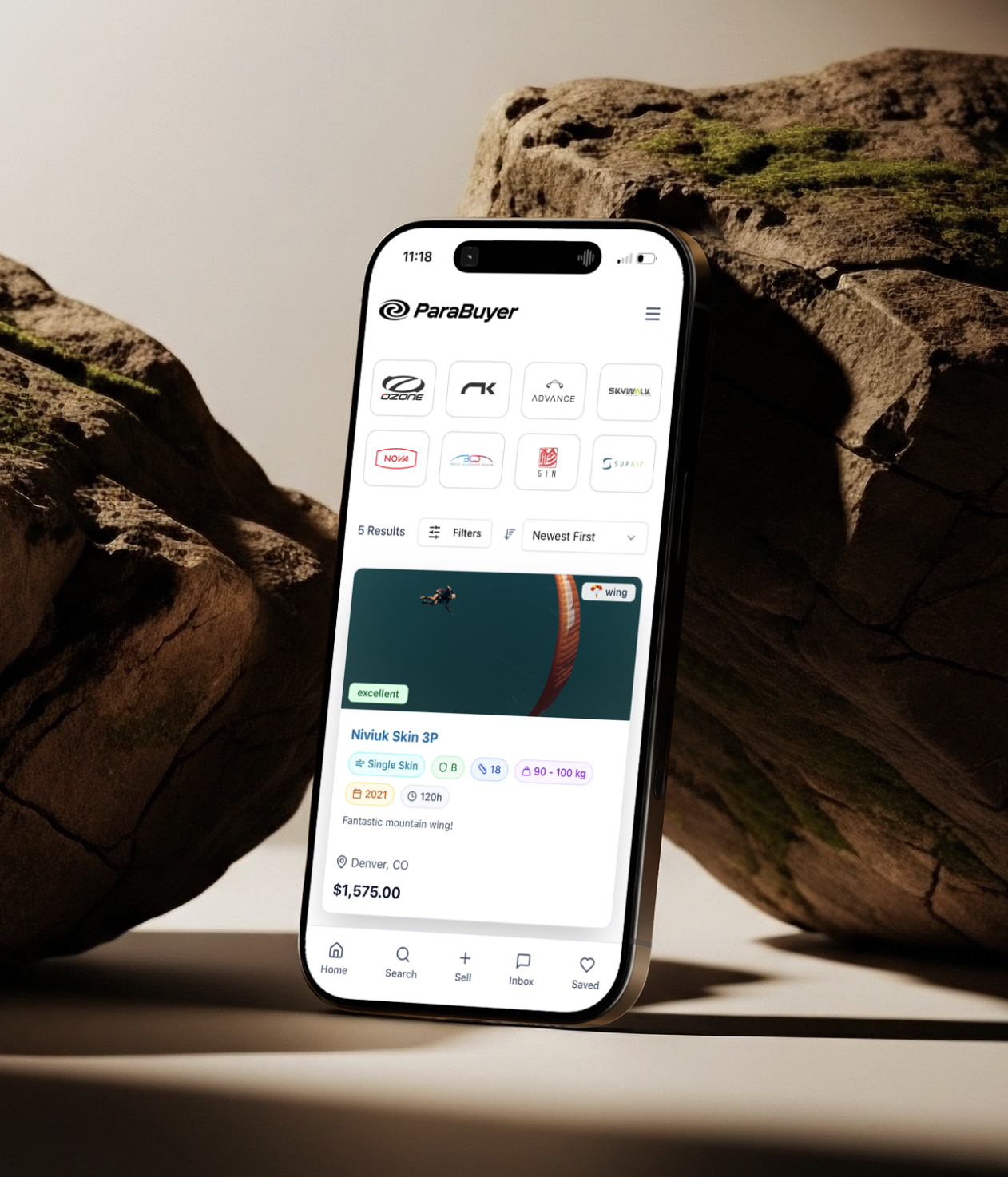 ParaBuyer browse screen — brand grid and Niviuk Skin 3P listing — on iPhone against weathered rock